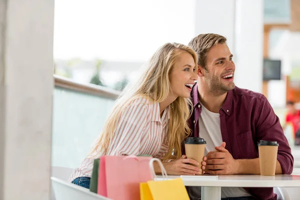 Rindo jovem casal sentado à mesa com café no café depois de fazer compras — Fotografia de Stock