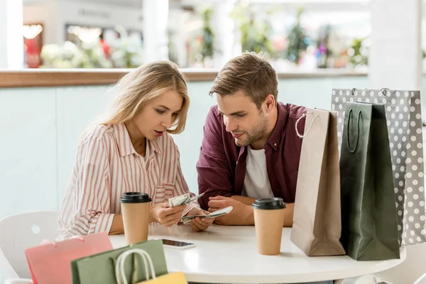 Focused young couple counting cash money at table with coffee cups in cafe — Stock Photo