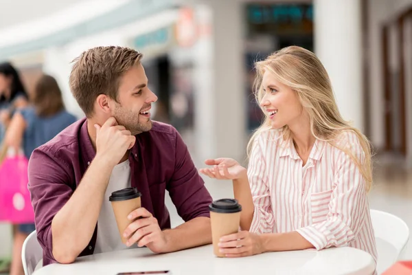 Mujer feliz con taza de papel de café gesto a mano y hablar con el novio en la mesa en la cafetería - foto de stock