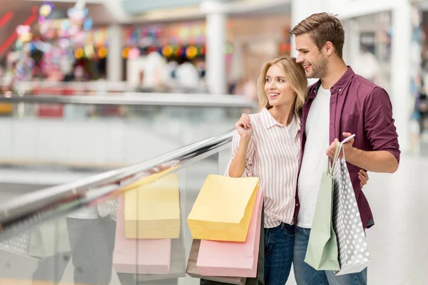 Enfoque selectivo de pareja con bolsas de compras y smartphone en el centro comercial - foto de stock