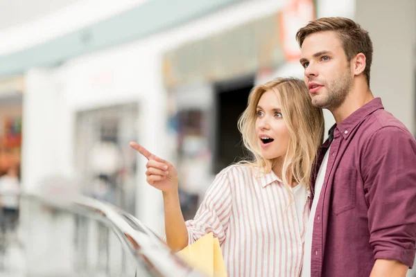 Selective focus of young woman with shopping bags pointing to boyfriend at shopping mall — Stock Photo