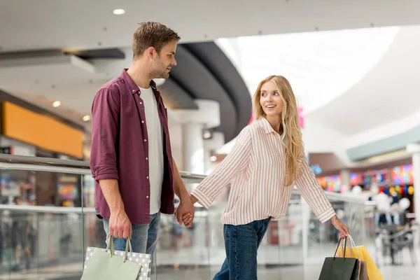 Enfoque selectivo de la joven pareja de compradores con bolsas de papel caminando en el centro comercial - foto de stock