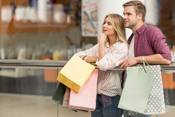 Couple souriant d'acheteurs avec des sacs en papier debout au centre commercial — Photo de stock