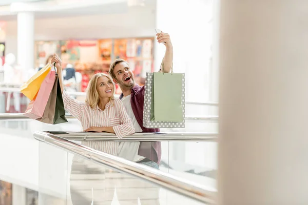 Enfoque selectivo de joven sonriente pareja de compradores con tomar selfie con bolsas de compras en el centro comercial - foto de stock