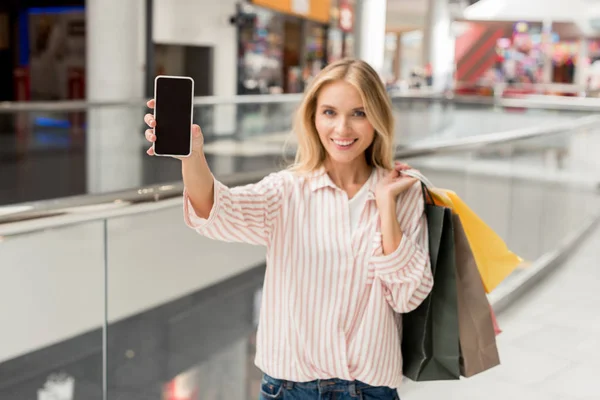 Selektiver Fokus der Frau mit Papiertüten zeigt Smartphone mit leerem Bildschirm in Einkaufszentrum — Stockfoto