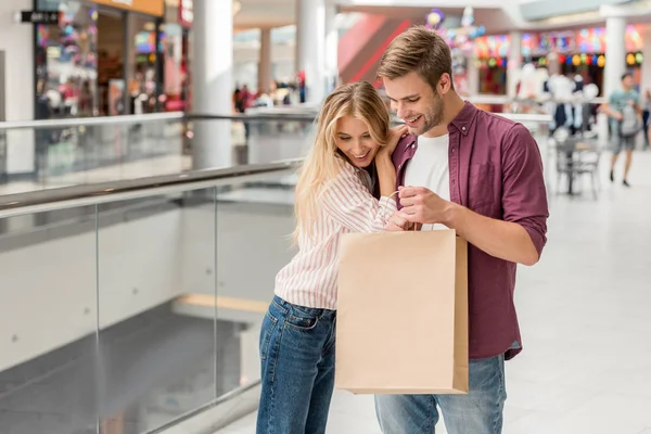 Couple of shoppers looking down and holding paper bag at shopping mall — Stock Photo