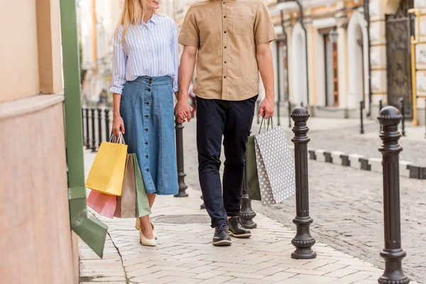 Vue partielle du couple élégant avec des sacs à provisions marchant dans la rue urbaine — Photo de stock