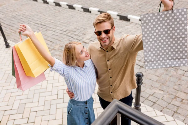 High angle view of excited couple with raised arms holding shopping bags at city street — Stock Photo
