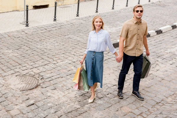 Високий кут зору на стильну пару покупців з паперовими мішками, що йдуть по міській вулиці — стокове фото