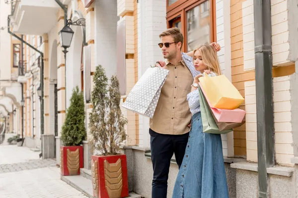 Jovem casal de compradores com sacos de papel posando na rua urbana — Fotografia de Stock