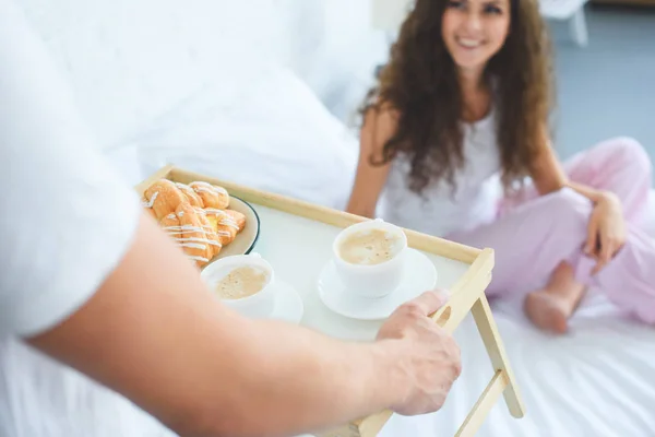 Teilbild eines Mannes, der seiner schönen lächelnden Freundin im Bett das Frühstück bringt — Stockfoto