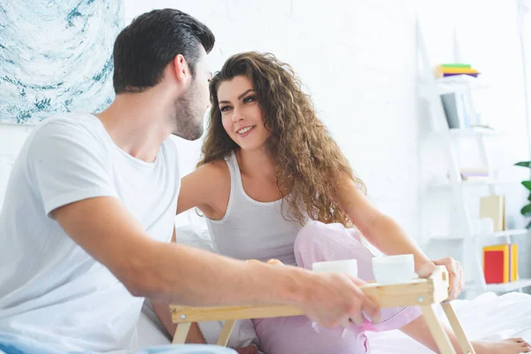 Felice giovane coppia sorridente mentre fa colazione insieme a letto — Foto stock