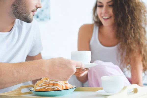 Recortado disparo de feliz joven pareja teniendo croissants y café para el desayuno en la cama - foto de stock