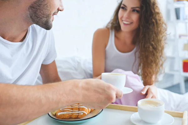 Recortado disparo de sonriente joven pareja teniendo croissants y café para el desayuno en la cama - foto de stock