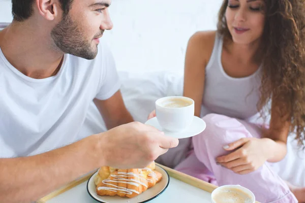 Cropped shot of young couple having croissants and coffee for breakfast in bed — Stock Photo