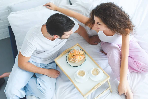 Вид сверху на молодую пару в пижаме, завтракающую вместе в постели — стоковое фото