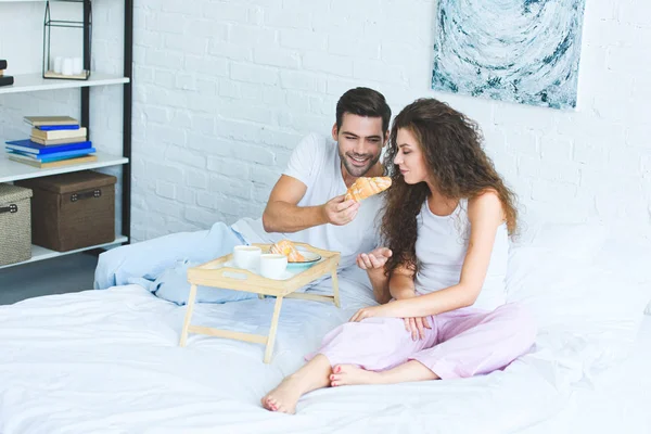 Blick aus der Vogelperspektive auf ein glückliches junges Paar im Pyjama beim gemeinsamen Frühstück im Schlafzimmer — Stockfoto