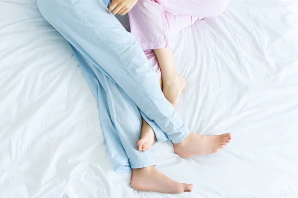 Seção baixa de jovem casal de pijama deitado juntos na cama — Fotografia de Stock