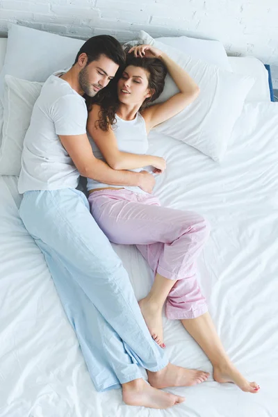 Вид сверху на красивую счастливую молодую пару в пижаме, лежащую вместе на кровати — стоковое фото