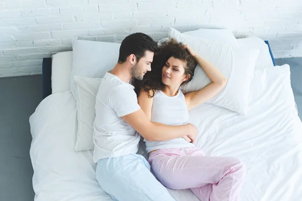 Vue de dessus du jeune couple heureux en pyjama couché ensemble sur le lit — Photo de stock