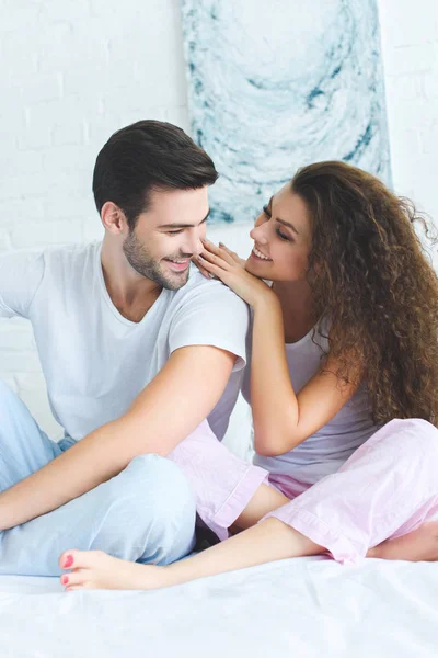 Красивая счастливая молодая пара в пижаме, сидящая вместе на кровати — стоковое фото