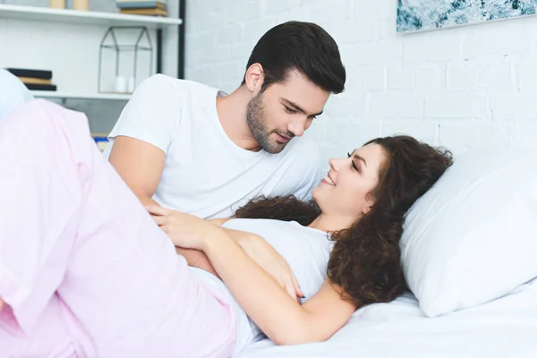 Щаслива молода пара в любові посміхається один одному, лежачи разом у ліжку — стокове фото