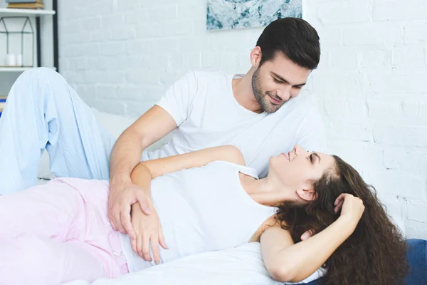 Bonito peludo jovem olhando para sorrindo namorada na cama — Fotografia de Stock