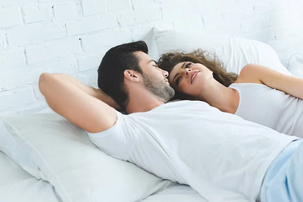 Schöner junger Mann, der die schöne lächelnde Freundin ansieht, während er zusammen im Bett liegt — Stockfoto