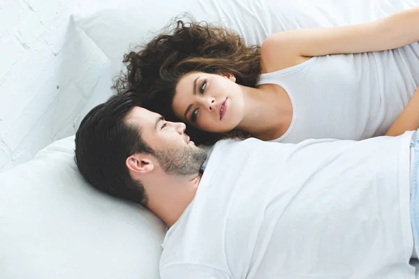 Vista de ángulo alto de hermosa pareja joven acostada en la cama y mirándose el uno al otro - foto de stock