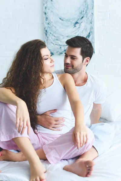 Счастливая молодая пара в пижаме, обнимающая кровать — стоковое фото