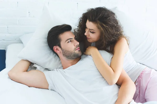 Vista de ángulo alto de hermosa pareja joven enamorada acostada en la cama y mirándose el uno al otro - foto de stock