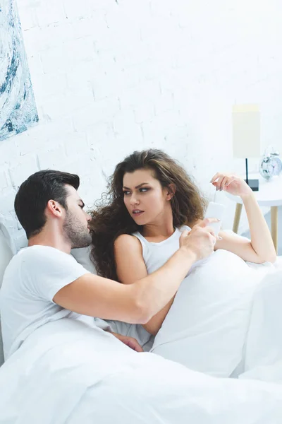 Vista de ángulo alto de pareja discutiendo sobre el teléfono inteligente en la cama, concepto de dificultades de relación - foto de stock