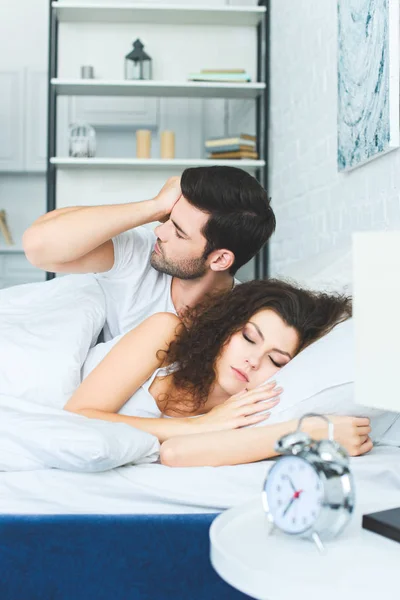 Young man waking up and rubbing eye while girlfriend sleeping in bed — Stock Photo