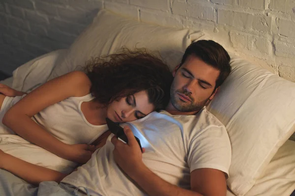 High angle view of young couple sleeping in bed, man holding smartphone — Stock Photo