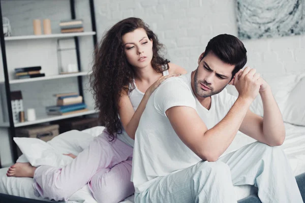 Girl looking at upset boyfriend sitting on bed, relationship difficulties concept — Stock Photo