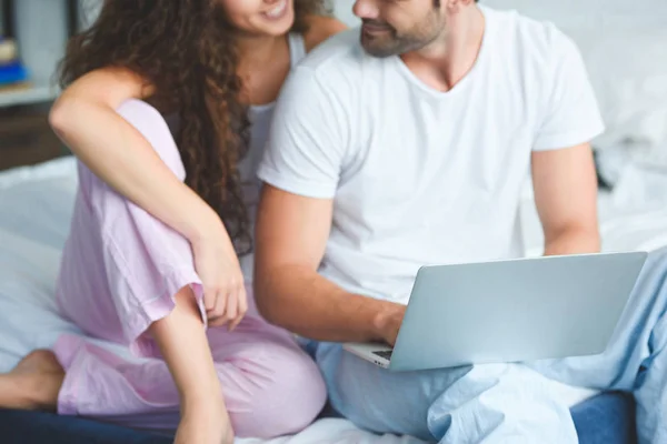 Schnappschuss eines lächelnden jungen Paares im Pyjama mit Laptop auf dem Bett — Stockfoto