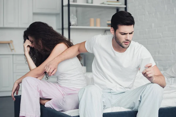 Unzufriedenes junges Paar streitet, während Mann Smartphone in der Hand hält, Beziehungsprobleme — Stockfoto