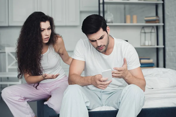 Sconvolto giovane coppia litigando mentre l'uomo utilizzando smartphone, concetto di difficoltà di relazione — Foto stock