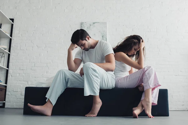 Низкий угол зрения расстроенной молодой пары в пижаме, сидящей спиной к спине на кровати — стоковое фото