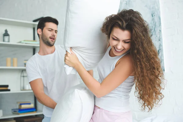 Young couple in pajamas having fun and fighting with pillows on bed — Stock Photo