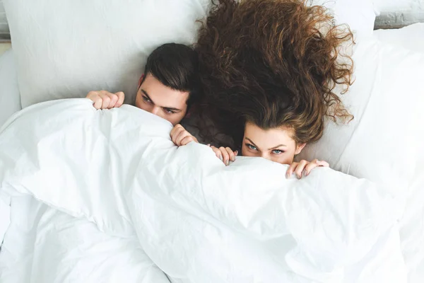 Draufsicht auf ein junges Paar, das unter einer weißen Decke im Bett liegt — Stockfoto
