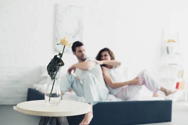 Rose flower in vase and young couple quarreling on bed behind — Stock Photo