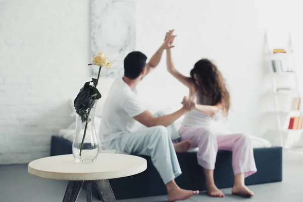 Flor de rosa en jarrón y joven pareja peleando en la cama detrás, concepto de dificultades de relación - foto de stock