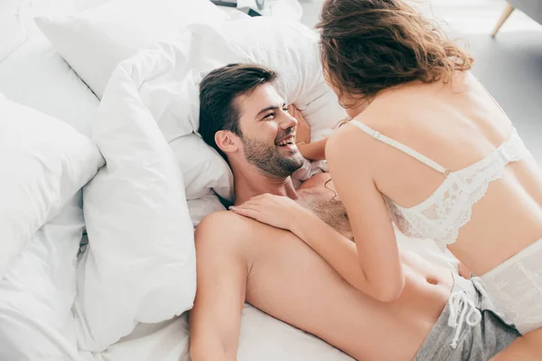 Високий кут зору усміхнений чоловік лежить на ліжку і дивиться на сексуальну дівчину в нижній білизні — стокове фото