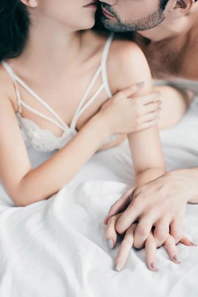 Schnappschuss von verführerischem jungen Paar, das sich Händchen hält und im Bett küsst — Stockfoto