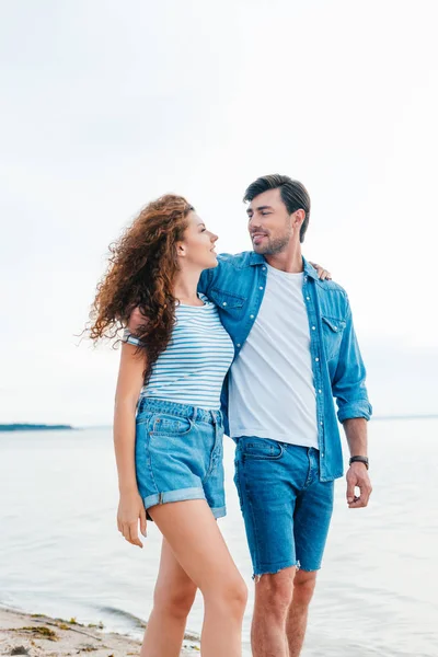 Hermosa novia y novio sonriente abrazándose en la orilla del mar - foto de stock