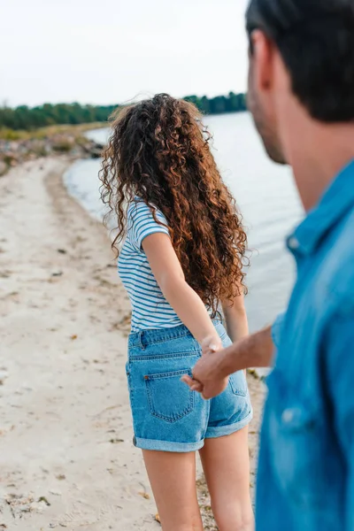 Young couple holding hands and walking on beach — Stock Photo