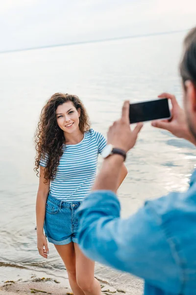 Hombre tomando foto de novia cerca del mar en el teléfono inteligente - foto de stock