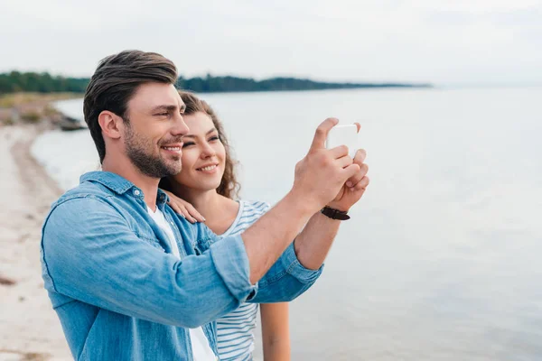 Красива усміхнена пара фотографує море на смартфоні — стокове фото