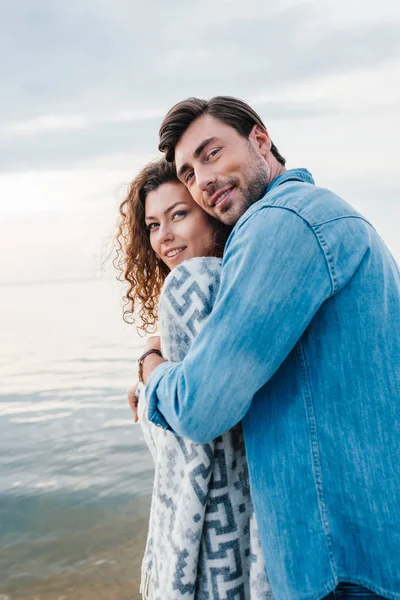 Homme heureux étreignant petite amie enveloppé dans la couverture — Photo de stock